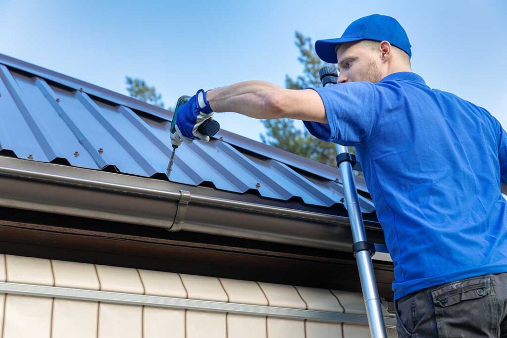 Person inspecting vented soffit panels and fascia boards along a home's roof edge in daylight