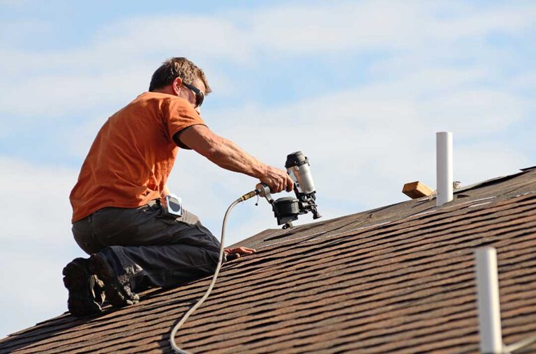 Homeowner inspecting roof shingles and gutters from the ground beside a house in autumn